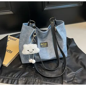 Détail du sac fourre-tout en denim bleu avec anses en cuir noir et breloque nuage doux