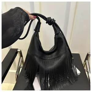 Detalle del cuero granulado negro y flecos largos y fluidos en un elegante bolso al hombro