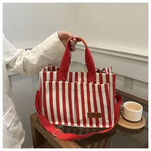 Detail view of red and white striped canvas tote with brown leather label and adjustable strap