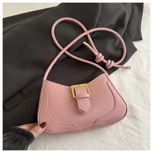 Détail d'un sac demi-lune rose avec boucle dorée sur un blazer noir et tissu texturé