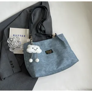 Détail du sac cabas en denim bleu avec breloque nuage en peluche sur une surface plane