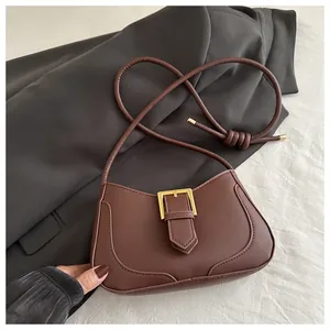 Détail d'un sac bandoulière marron en forme de croissant avec boucle dorée et cuir mat
