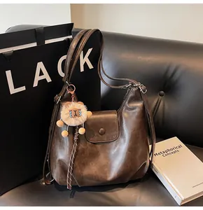 Close-up of brown tote bag with lion plush pendant on a leather sofa surface