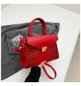 Détail du sac à main rouge style enveloppe avec boucle dorée et texture crocodile