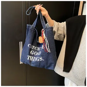 Detail of dark blue denim tote bag with white letter print and brown plush bear charm