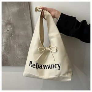 Detail of cream canvas tote bag featuring Rebawancy lettering and decorative bow tie