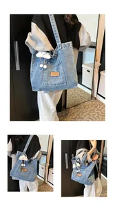Detail of washed light blue denim tote bag with brown leather tag and smiley cloud charm