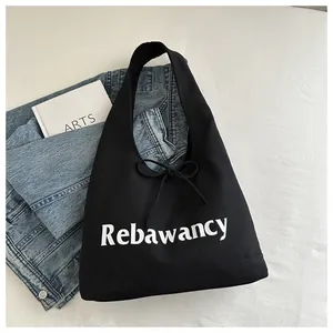 Close-up of black canvas tote bag with white Rebawancy text and decorative bow detail