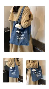 Detail of blue denim tote bag featuring white slogan and plush cloud keychain pendant