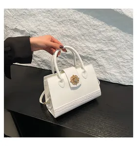Detail of white leather handbag featuring crocodile embossing and gold floral metal lock