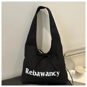 Detail of black canvas tote bag featuring white logo lettering and bow tie decoration