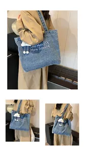 Detail view of denim tote bag with white embroidery and cloud plush charm accessory