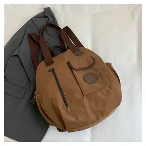 Detail of brown nylon travel bag featuring a front pocket with round logo and metal zippers