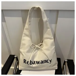Detail of minimalist cream canvas tote bag featuring a bow tie and black letter print
