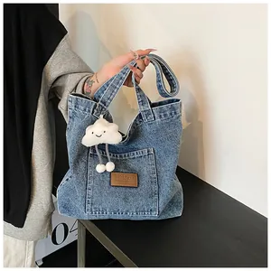 Detail of blue denim tote bag with leather logo patch and white cloud plush charm