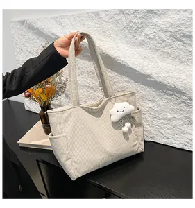 Detail of beige corduroy tote bag showing side pocket and white cloud plush charm