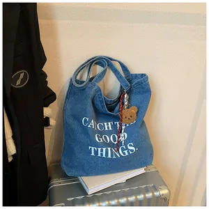 Detail of blue denim tote bag with white text print and a cute brown plush bear charm