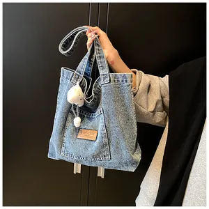 Detail of blue denim tote bag with brown leather patch and white plush pompom charm