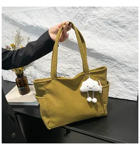 Close-up of olive green corduroy tote bag with plush cloud charm and side pocket