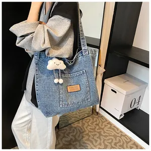 Detail of blue denim tote bag featuring a branded leather patch and cloud plush charm