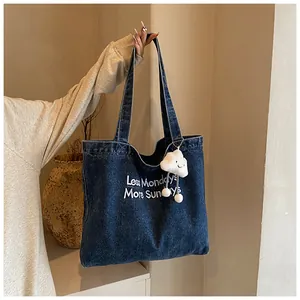 Detail of blue denim tote bag with Less Mondays More Sundays white embroidery and cloud charm