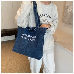Detail of dark blue denim tote bag with 'Less Mondays More Sundays' text and wide strap