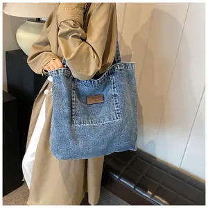 Detail of blue denim tote bag featuring a front pocket and brown leather brand label