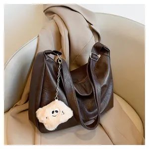 Detail of vintage dark brown leather tote bag with a white plush charm on a grey chair