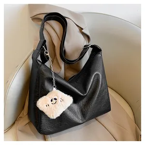 Detail of black tote bag on white chair with plush smiley face charm and matte leather texture