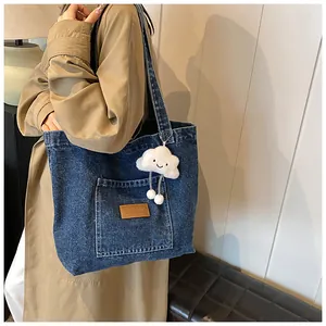 Detail of blue denim tote bag featuring a leather logo patch and cute cloud plush charm