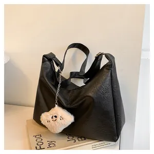 Detail of black tote bag featuring wrinkled leather texture and a plush bear charm