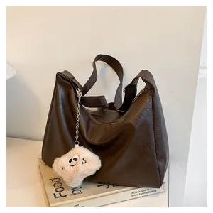 Detailed view of dark brown textured leather tote bag with a soft cloud charm on a book
