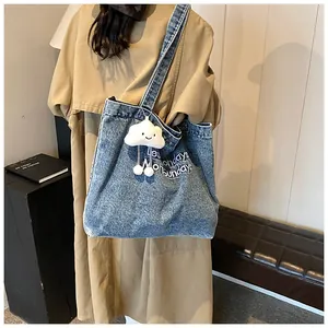 Detail of blue denim tote bag with white plush cloud charm and embroidered text design