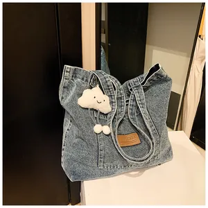 Detail of blue washed denim tote bag featuring a leather patch and white plush charm