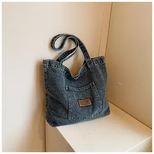 Close-up of vintage blue denim tote bag featuring a leather logo patch and outer pocket