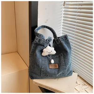Detail of blue denim tote bag featuring a leather logo patch and cloud plush charm