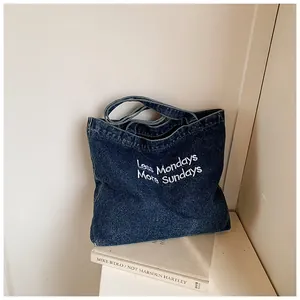 Detail of dark blue denim tote bag with Less Mondays More Sundays text embroidery