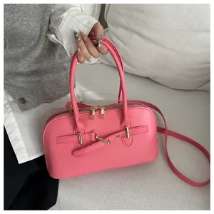 Detail van helderroze tas met gouden hardware en leren riem op een witte bank