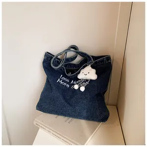Detail of blue denim tote bag with Less Monday More Sunday white embroidery and cloud charm
