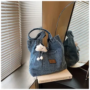 Detail of blue denim tote bag featuring a leather logo patch and cloud plush charm decoration