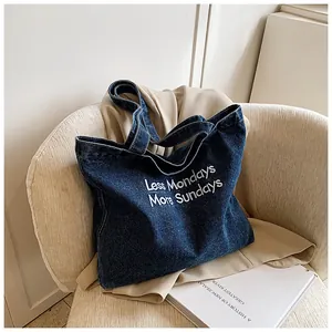 Detail of blue denim tote bag with white embroidery on a casual fabric chair