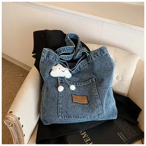 Detail of blue denim tote bag with brown leather logo patch and white plush cloud charm