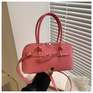 Detail van een roze handtas in schelpvorm met gouden hardware en verstelbare schouderriem