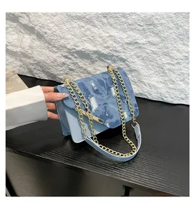 Close-up of blue denim and leather patchwork crossbody bag with metallic chain detail