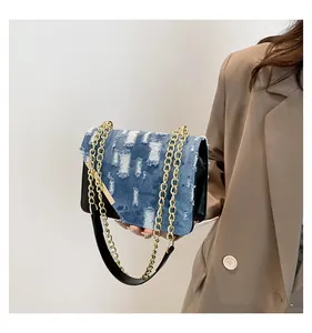 Close-up of distressed denim shoulder bag with vintage wash and gold chain strap detail