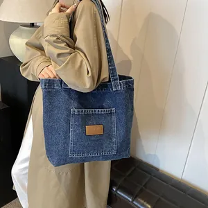 Vintage dark blue denim tote bag with leather patch on a model in a warm interior