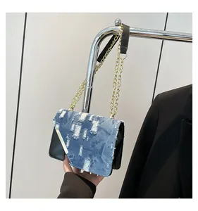 Detail view of denim and black leather patchwork bag with gold chain and metal trim