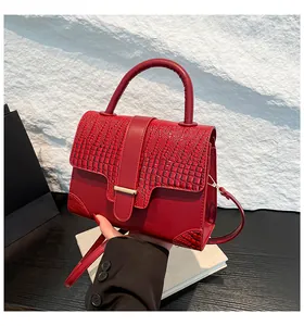 Detail view of red crocodile pattern handbag with metal buckle and textured flap