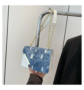 Detail of blue denim patchwork bag with frayed edges and golden metal chain strap