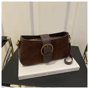 Détail d'un sac porté épaule en daim marron foncé avec boucle dorée sur un livre blanc